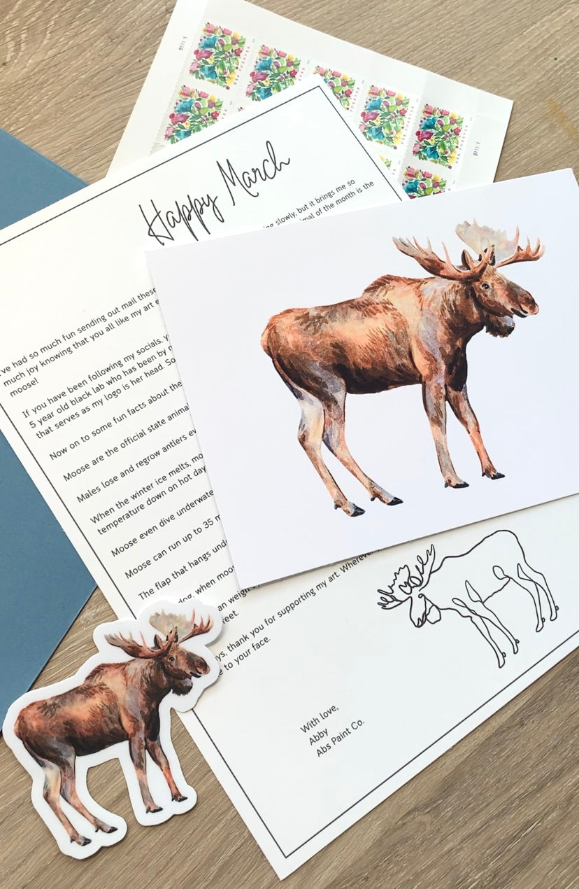 Moose-themed stationery set with letter, envelope, and stickers on a wooden surface.