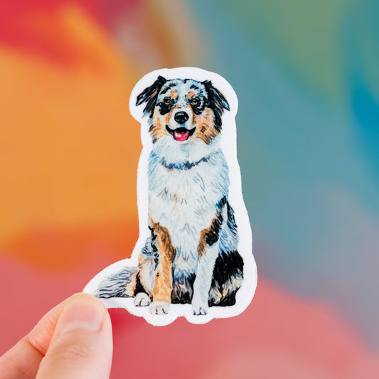 Sticker of an Aussie dog held by a hand with a colorful blurred background