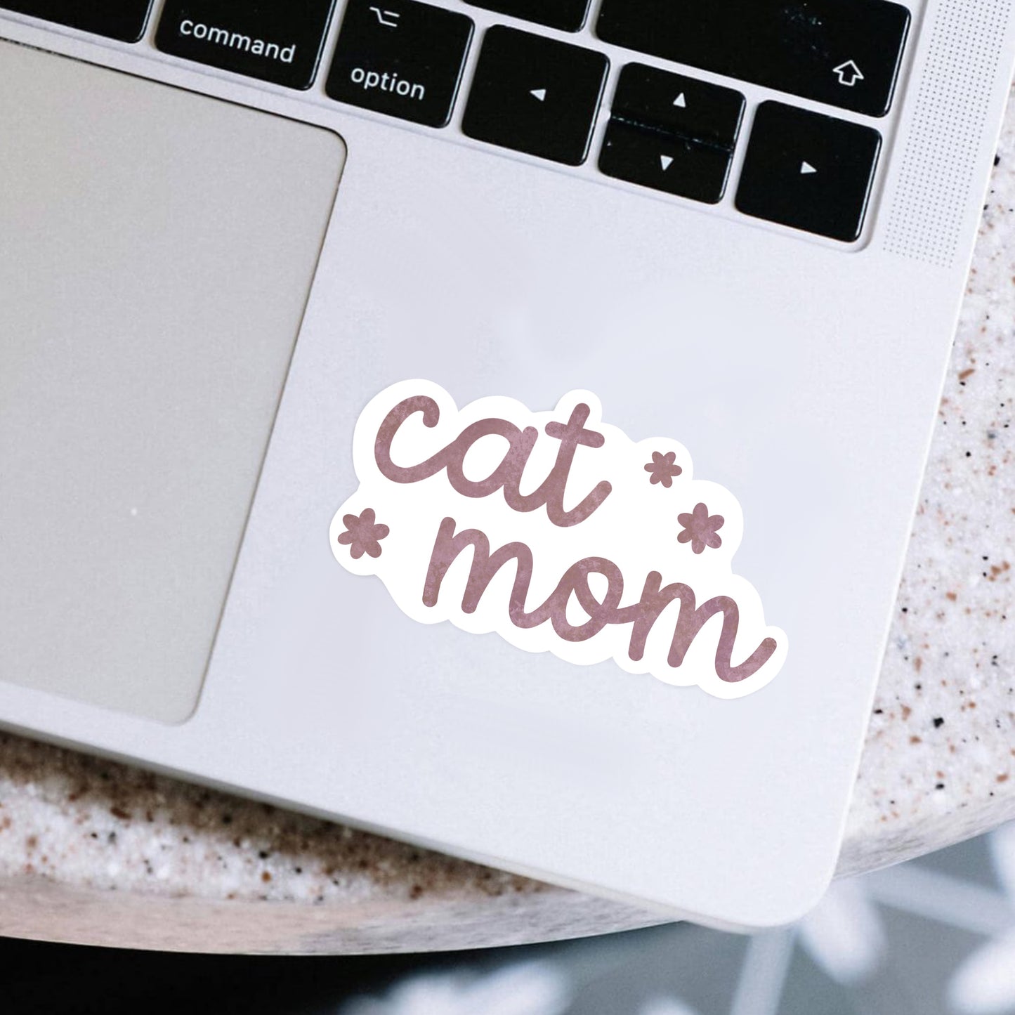 Laptop with a 'cat mom' sticker on a speckled surface