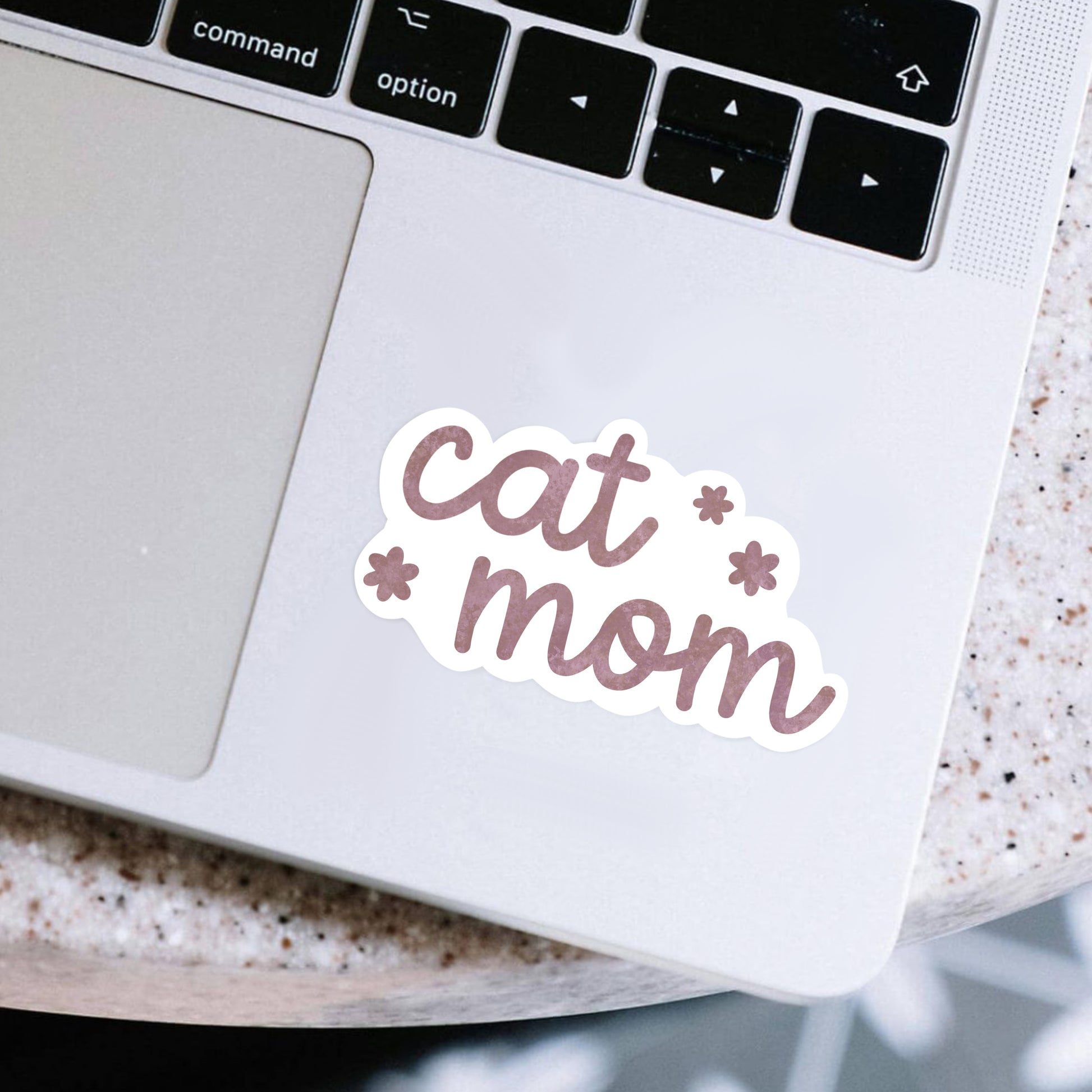 Laptop with a 'cat mom' sticker on a speckled surface