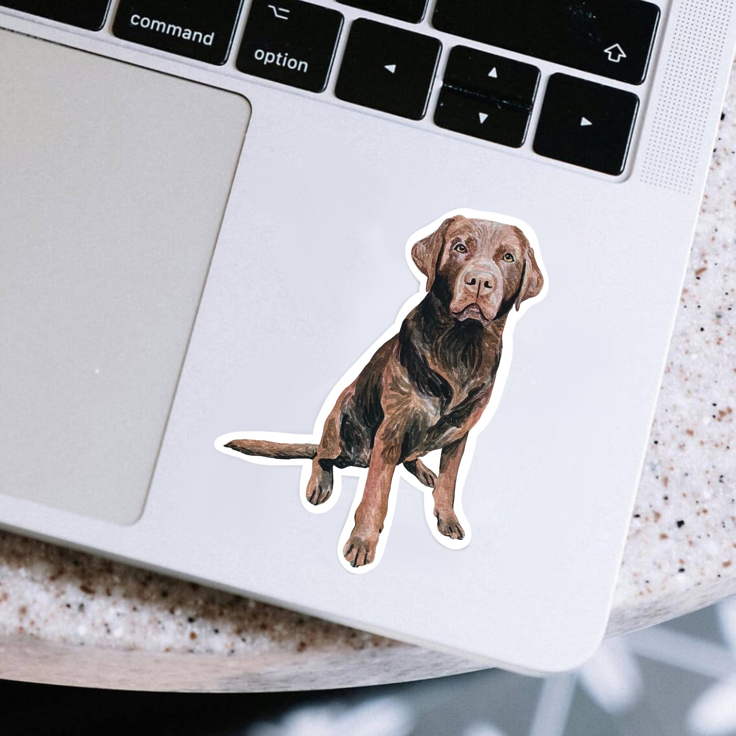 Laptop with a sticker of a chocolate lab dog on a speckled surface