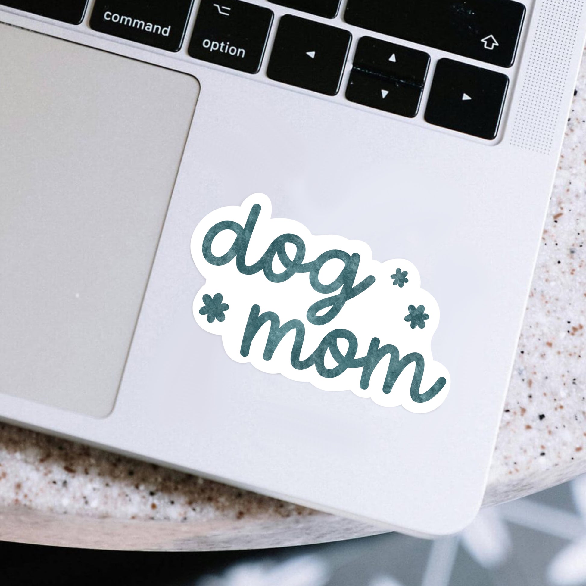 Laptop with a 'dog mom' sticker on a speckled surface