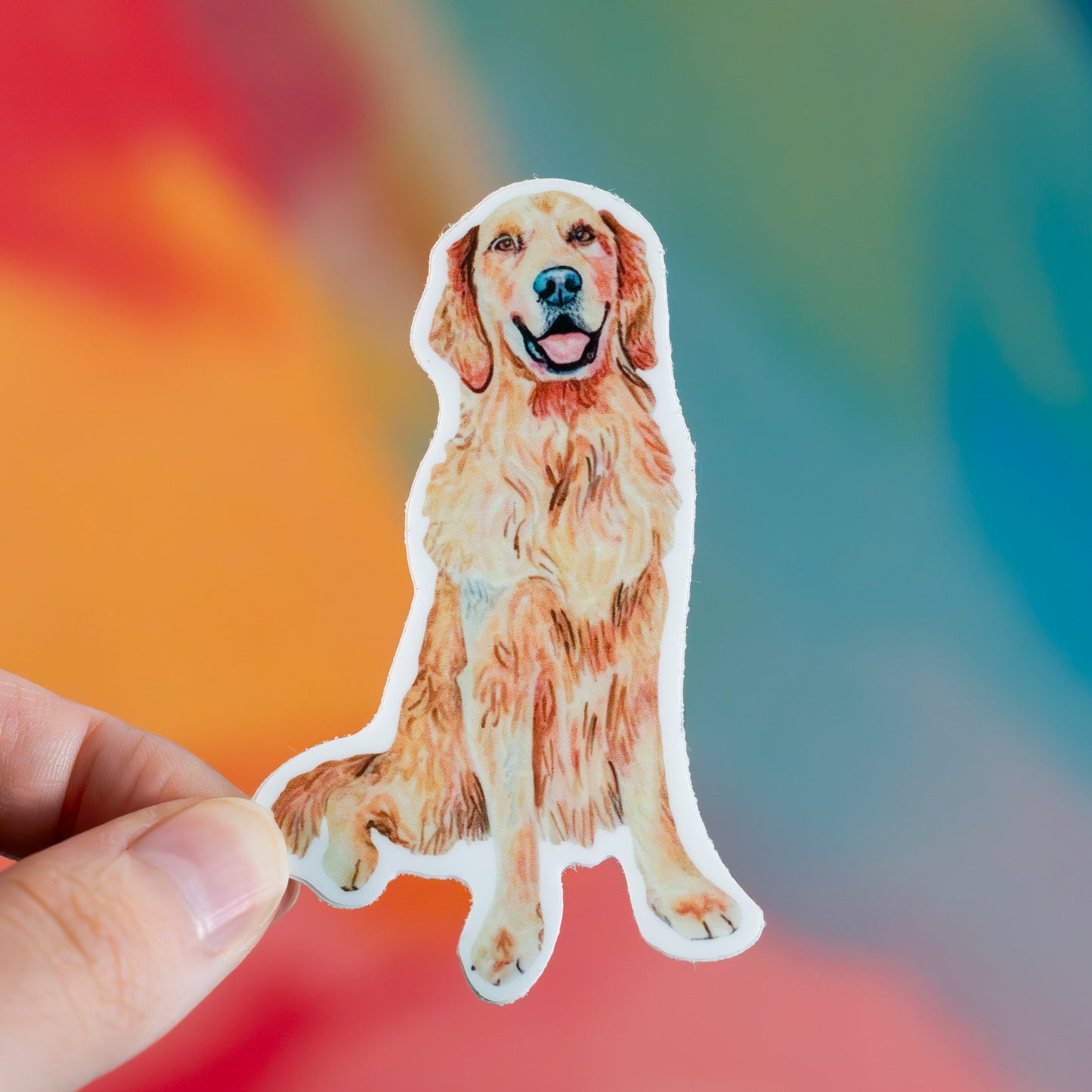 Hand holding a sticker of a golden retriever against a colorful background