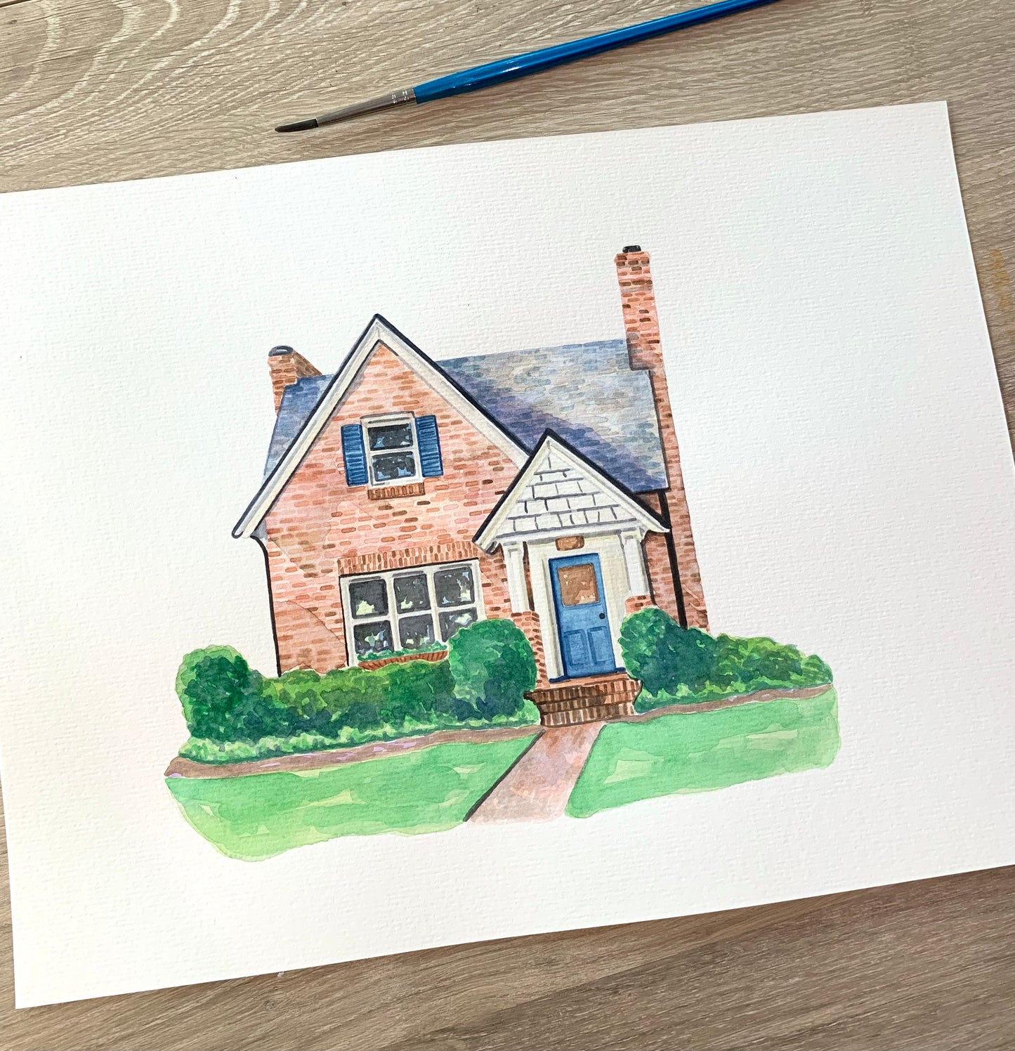 Hand-painted watercolor illustration of a brick house with a blue door, green bushes, and a white framed window.