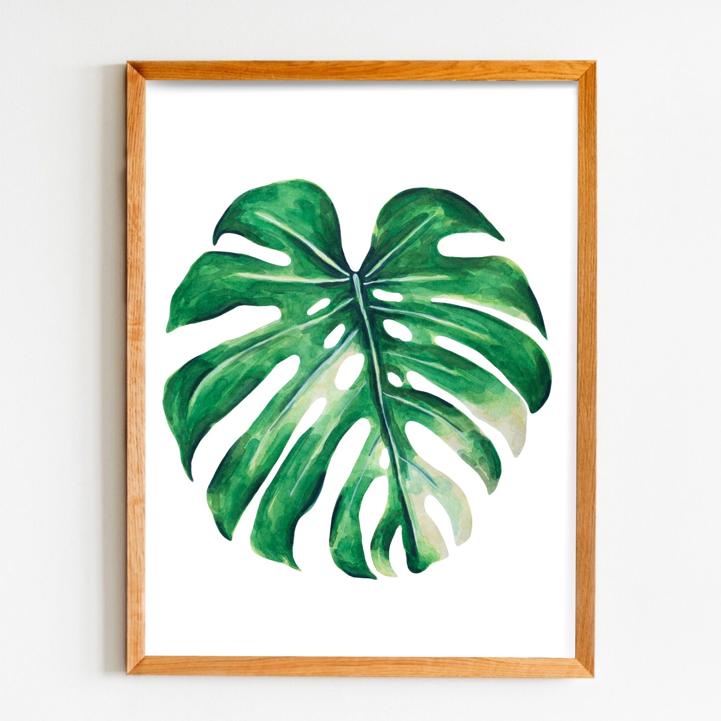 Framed artwork of a monstera leaf on a white wall