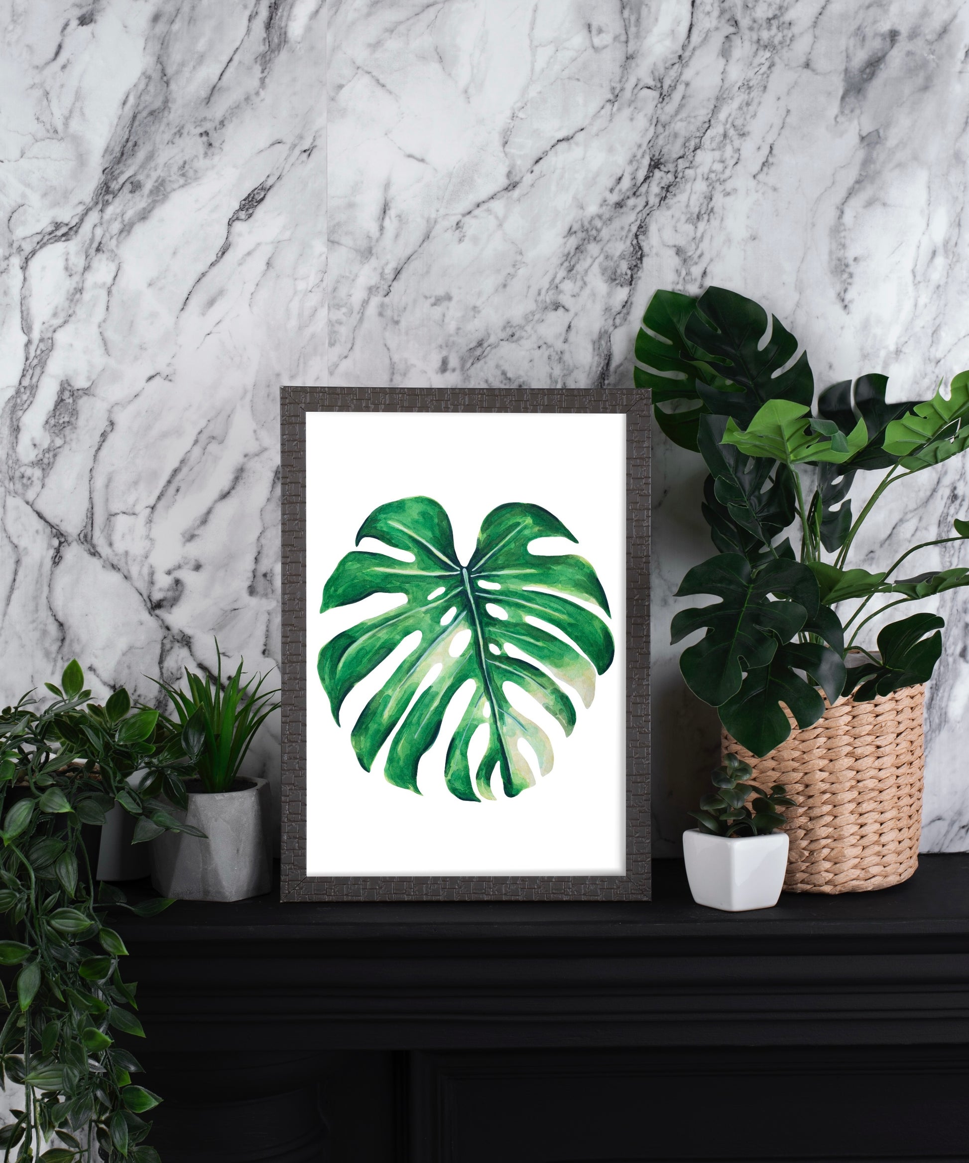Framed monstera leaf print on a shelf with plants against a marble wall.