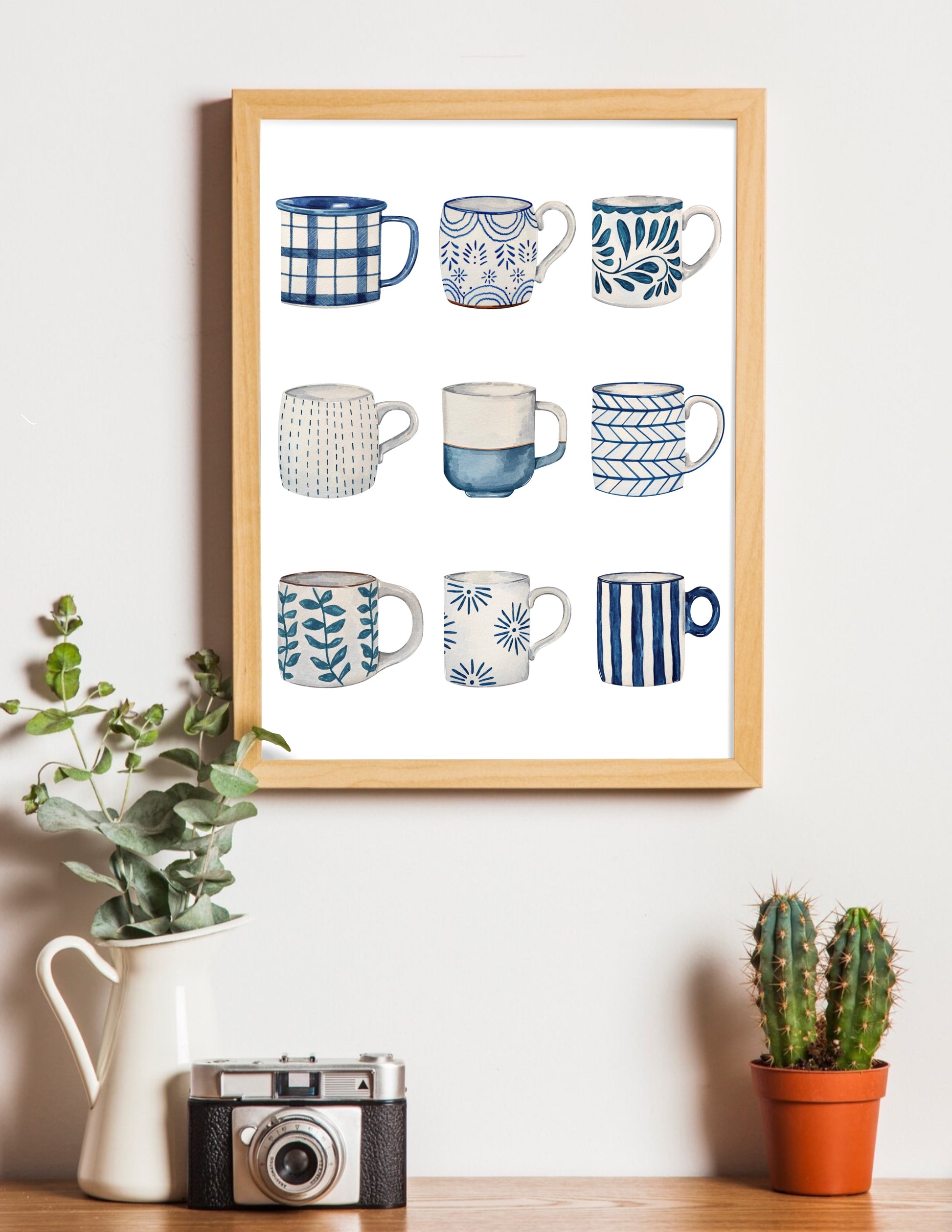 Framed artwork of various blue and white mugs on a wall with decorative items below.
