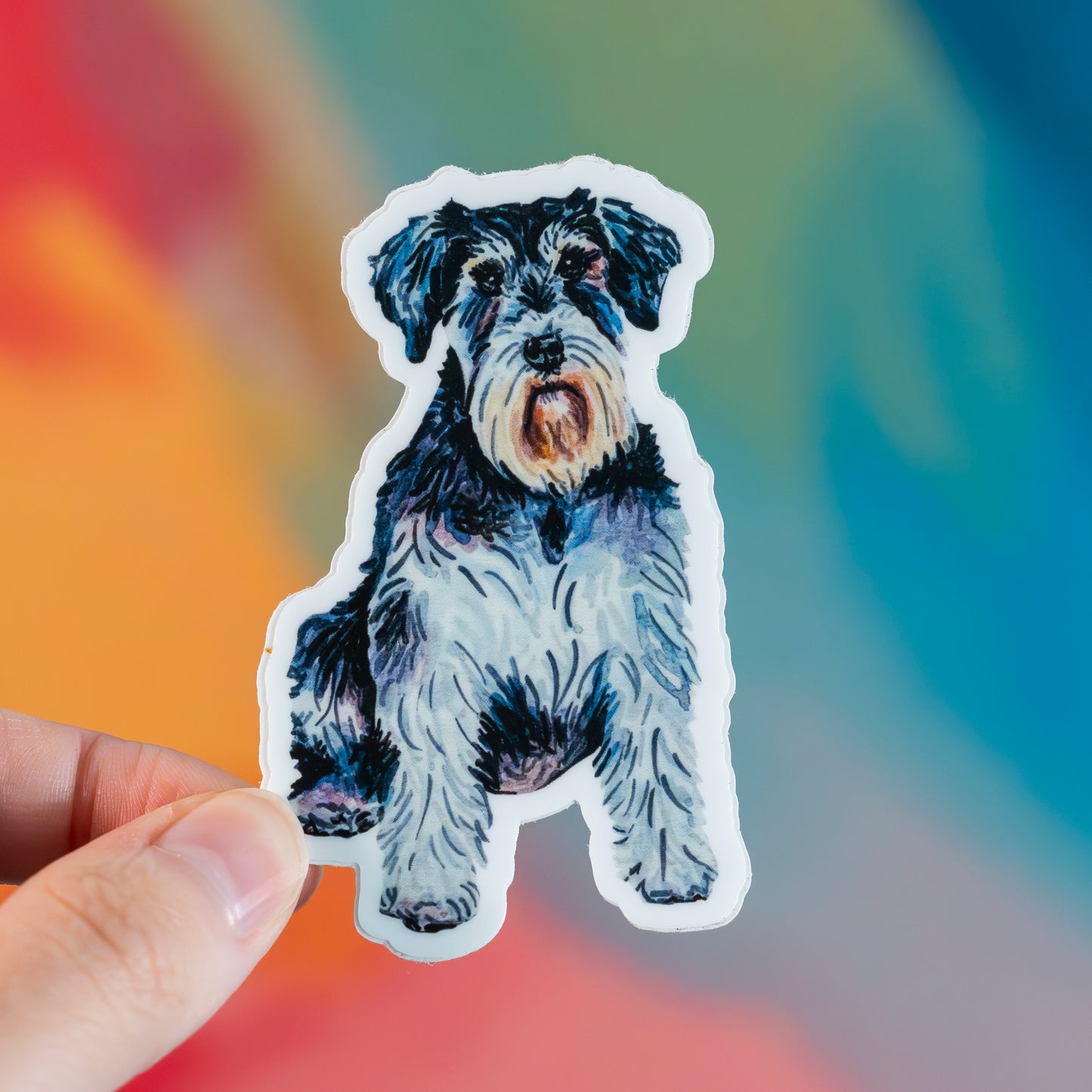 Sticker of a schnauzer dog held by a hand with a colorful blurred background