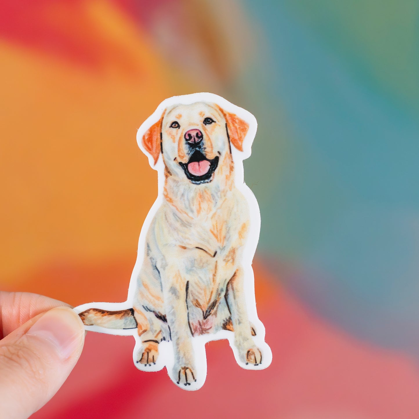 Sticker of a yellow lab dog held by a hand with a colorful blurred background